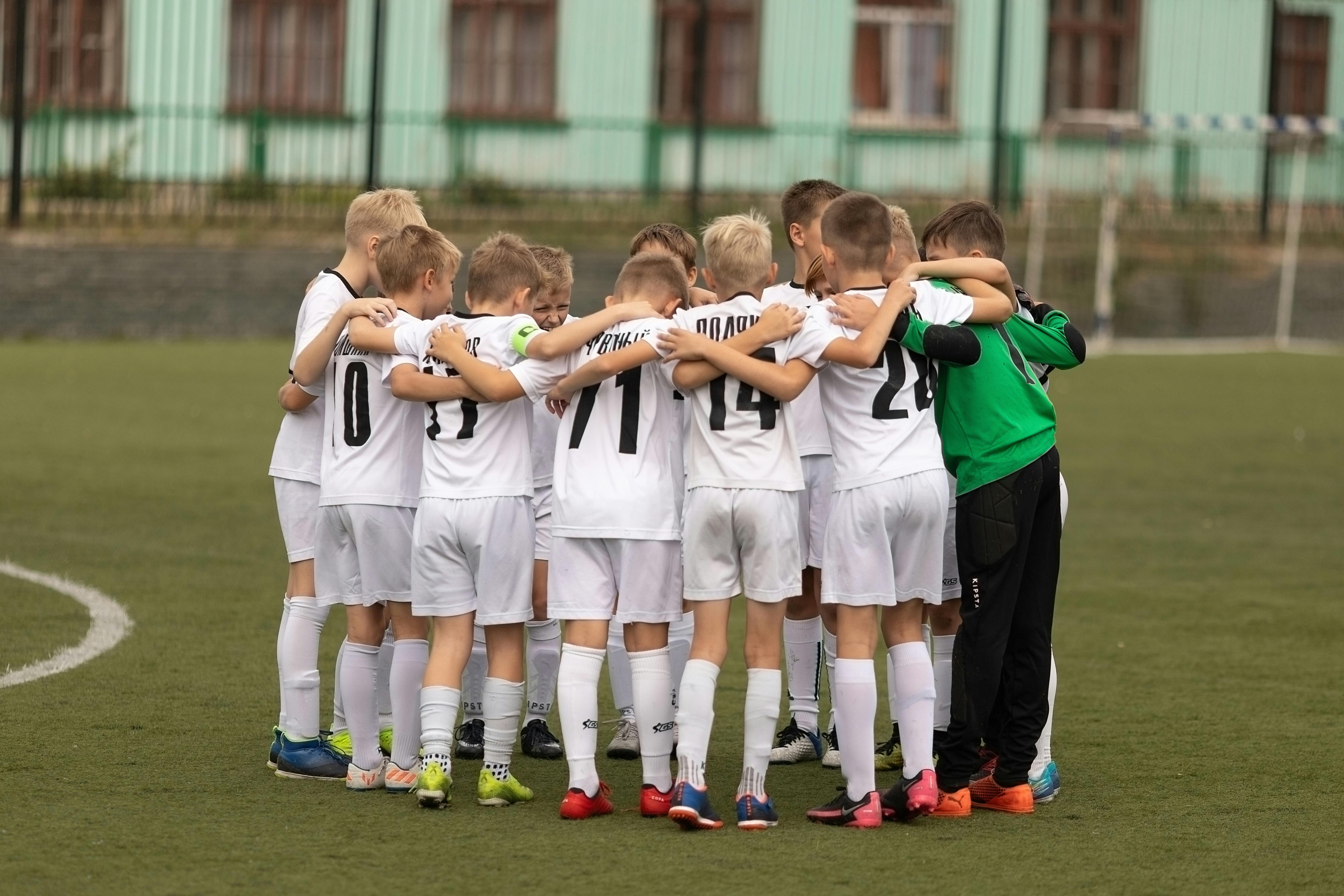 A youth soccer team in white jerseys huddling together.